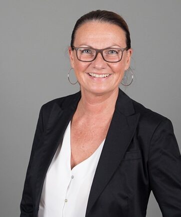 Eine Frau mit Brille und Blazer posiert für ein Foto.
